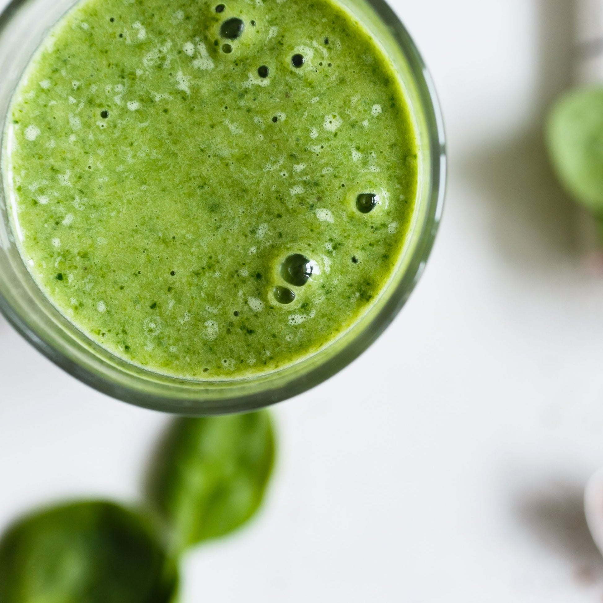 Close-up of a green smoothie in a glass with spinach leaves on a white background