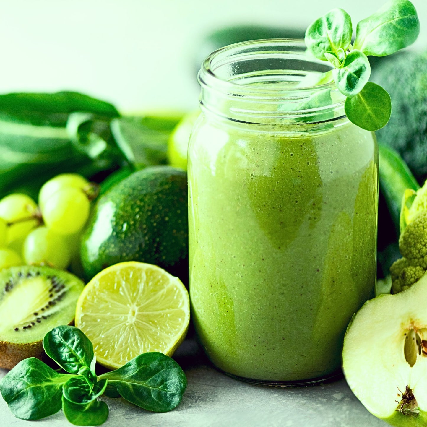Green smoothie in a jar surrounded by green fruits and vegetables on a light background