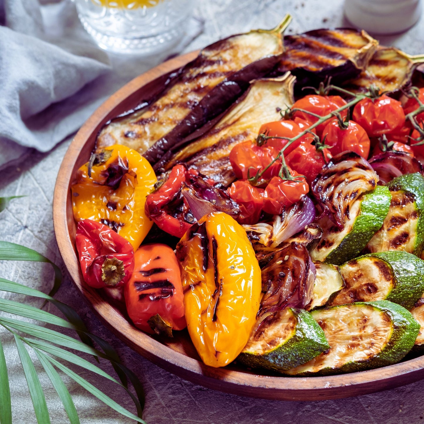 Assorted grilled vegetables including eggplant, zucchini, bell peppers, and tomatoes on a wooden plate.